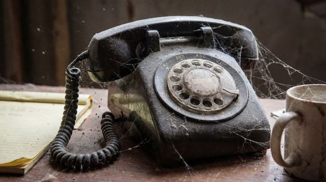 Vintage rotary telephone sitting under cobwebs on dusty wooden desk, relic of past era