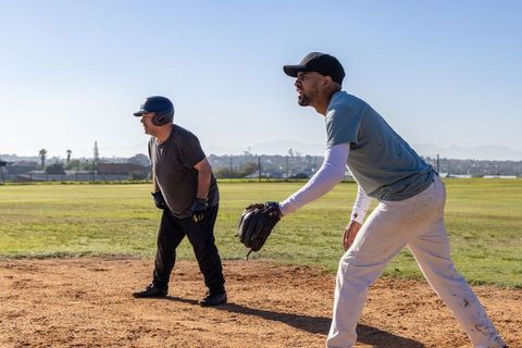 Coaching first base and guiding runner at neighborhood baseball field on sunny day