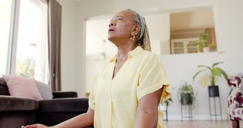 Senior African American Woman Meditating at Home in Yellow Shirt