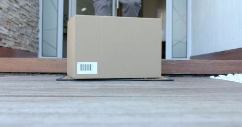 Parcel with barcode sitting on doormat at home porch with delivery person standing inside