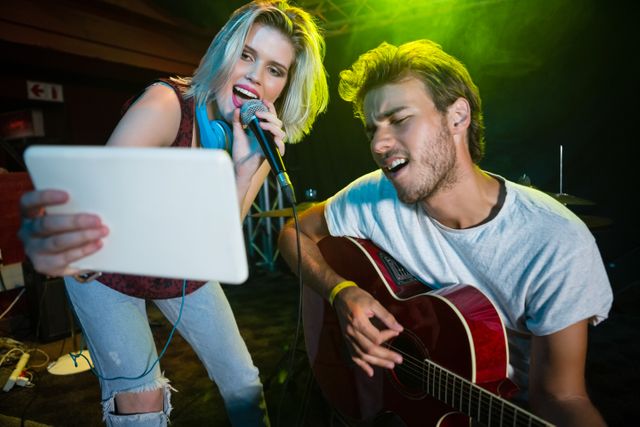 A lively image depicting a young band performing on stage in a vibrant nightclub. The female vocalist is energetically singing into the microphone while one of the band members passionately plays the guitar. Ideal for use in promotions for live music events, nightlife advertisements, concert flyers, and entertainment blogs highlighting live performances and nightlife experiences.