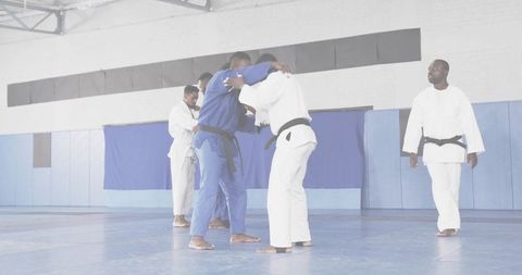 Judo pairs practicing clinch on blue dojo mats wearing gis and black belts