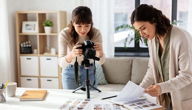 Two women adjusting dslr and reviewing contact sheets in bright home studio for content
