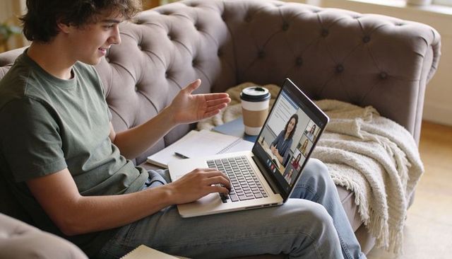 Joining remote class on laptop from cozy living room sofa, taking notes and chatting