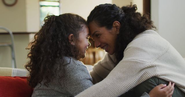 Mother and daughter with curly hair are smiling and embracing indoors. Use for family bonding, parent-child relationships, and lifestyle themes.