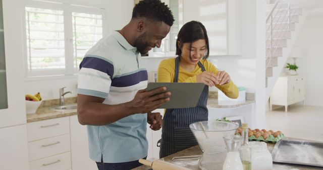 Happy diverse couple using tablet and baking in kitchen. Spending quality time at home concept.