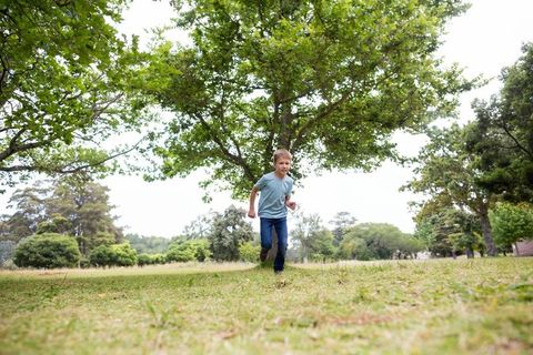 Energetic Boy Running in Lush Park with Leafy Trees