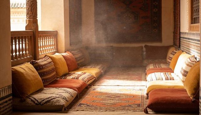 Sunlit moroccan riad alcove with low floor cushions, patterned kilim rugs and woodwork