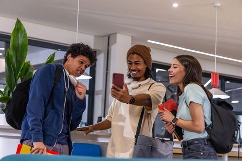 University students laughing while sharing smartphone in modern campus lounge
