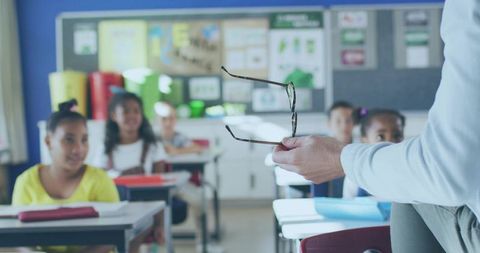 Teacher holding glasses addressing diverse elementary students in bright classroom