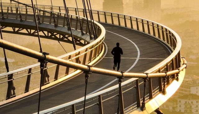 Jogging on sunlit curved bridge at sunrise silhouette runner over urban skyline
