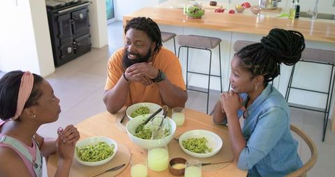 African american family sharing homemade pesto pasta around modern kitchen table
