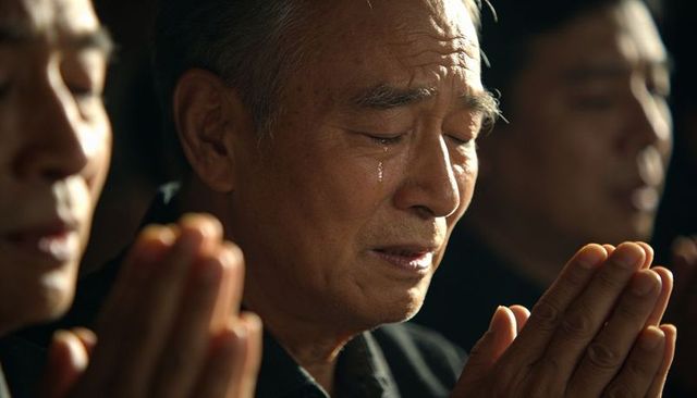 Elderly asian man praying, clasping hands and shedding tear in solemn worship closeup