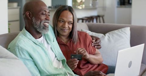 Mature african american couple smiling while shopping online with laptop and credit card