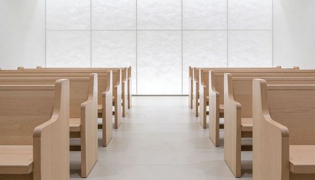 Minimalist chapel interior featuring light wooden pews and symmetrical central aisle
