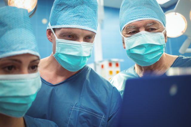Medical professionals in an operating room discussing patient information on a clipboard. Ideal for use in healthcare, medical training, hospital advertisements, and articles about surgical procedures and teamwork in healthcare settings.
