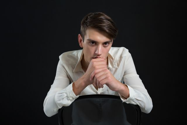 Portrait of androgynous man sitting on chair with hand on his chin