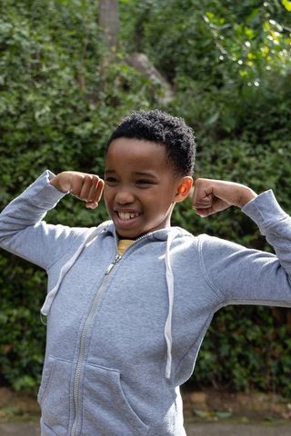 African american schoolboy flexing and smiling outdoors in gray hoodie and yellow shirt