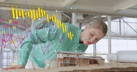 A serious female architect in contemporary attire reviews architectural models with floating financial graphs and data. The merging of professional expertise and technology reflects the increasing significance of digital tools in the modern global business environment. Useful for illustrating concepts of innovation in architecture, the impact of digital technologies on professions, and the role of data in decision-making processes.