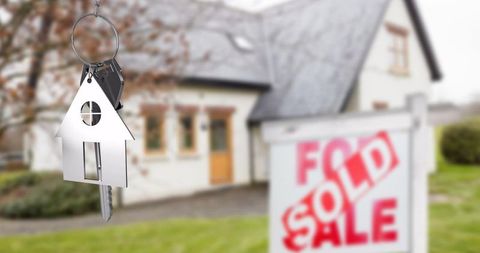 House-shaped key fob dangling over sold real estate sign homeownership closing