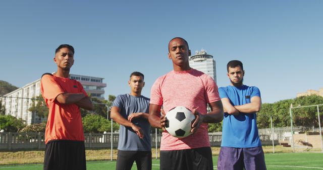Portrait of diverse male football players holding ball on outdoor pitch. Football, sports and teamwork.