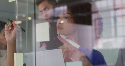 Team Collaborating Writing Ideas on Glass Board in Office