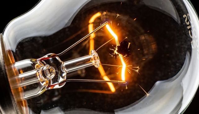 Sparking broken tungsten filament glowing inside clear incandescent bulb macro close-up
