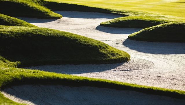 Sunlit golf course bunkers with raked sand patterns and sculpted grass mounds
