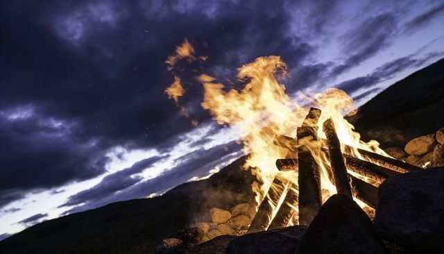 Bonfire burning on rocky hillside at dusk casting dramatic twilight glow and sparks