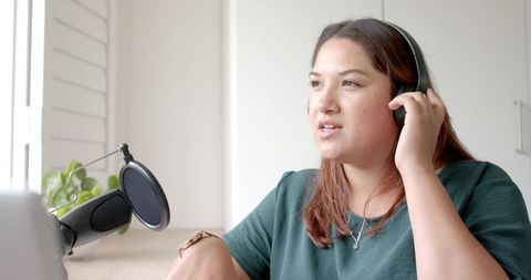 Biracial woman podcasting with headphones at home workspace