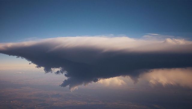 Towering Cumulonimbus Cloud Over Sunlit Fields and Rural Roads