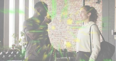 Fitness partners chatting and hydrating in modern gym with dumbbells, kettlebells, brick wall