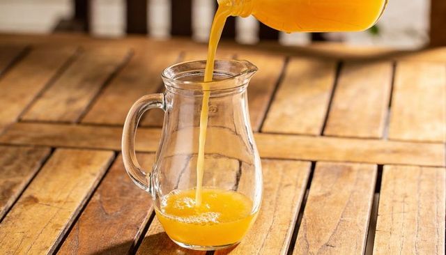 Pouring fresh orange juice into glass pitcher on rustic wooden table for serving