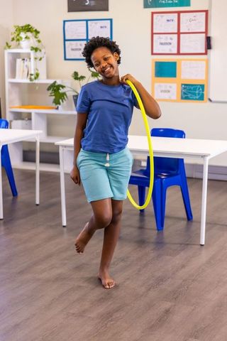 Smiling african american child holding yellow hula hoop balancing in modern classroom