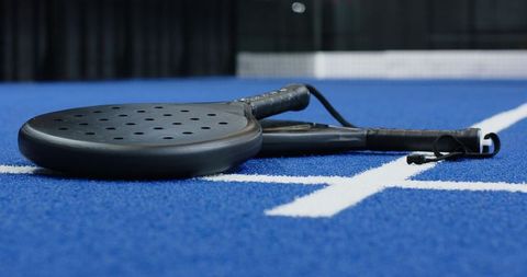 Black padel rackets resting on blue turf court