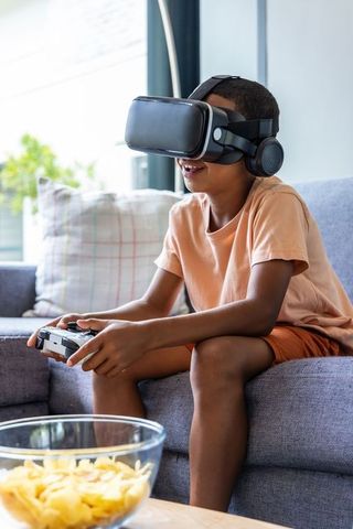 Young boy playing virtual reality game on couch with controller and headphones