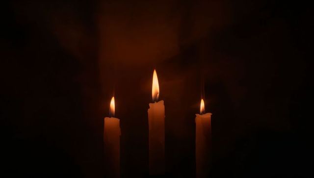 Three taper candles burning with warm halo and dripping wax in dark moody ambience