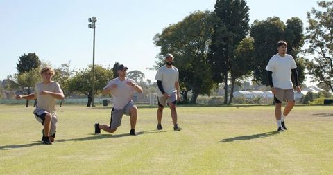 Diverse young men performing lunges in sunny park for group fitness training