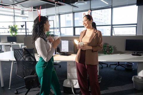 Two diverse female coworkers chatting and drinking coffee during holiday office break