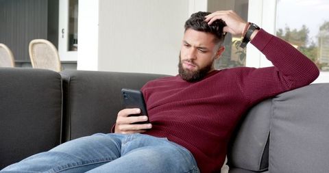 Young Man Pensive Using Smartphone on Cozy Living Room Sofa
