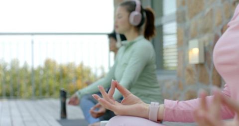Diverse women meditating on outdoor deck wearing headphones practicing mindfulness