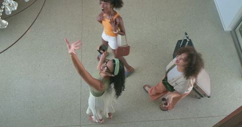 Young african american women reaching toward chandelier in hotel lobby with luggage
