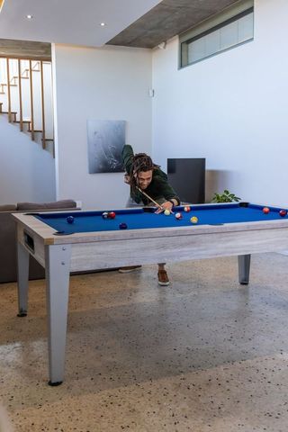 African american man playing pool on blue-felt table in modern minimalist home lounge