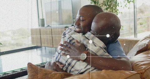 Black father and son hugging on tan couch in cozy modern living room, family bonding