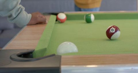 Diverse friends leaning on pool table rail watching billiards play on green felt