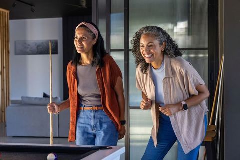 Two african american women leaning and lining up pool shot in contemporary home