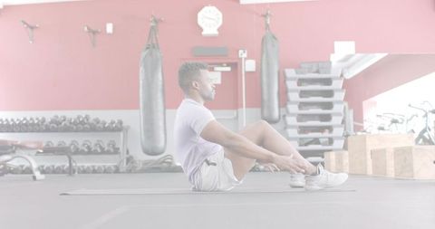 Performing seated crunches for core strength in modern gym with weights and punching bag
