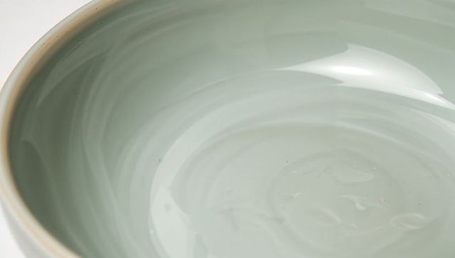 Celadon glazed shallow ceramic bowl with soft swirl glaze and beige rim for tableware