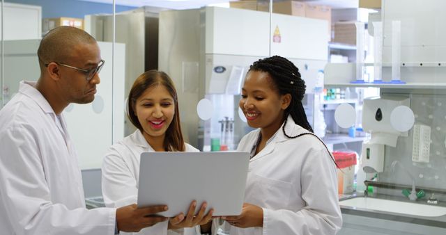 A diverse group of medical professionals, including African American and Hispanic individuals, are engaged in discussion over a laptop in a laboratory setting. Their collaboration involves research or analysis of medical data, emphasizing the importance of teamwork in healthcare.