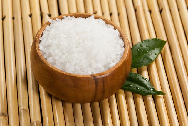 Sea salt in a wooden bowl with green leaves on a bamboo mat. Ideal for use in wellness, spa, and beauty-related content. Perfect for promoting natural and organic products, relaxation, and holistic health practices.